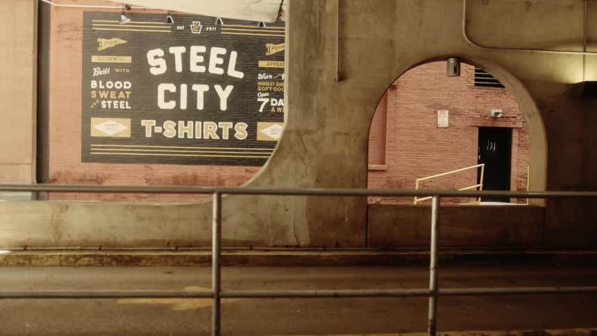 An urban scene with a concrete overpass and a brick building with a painted advertisement over a brick wall