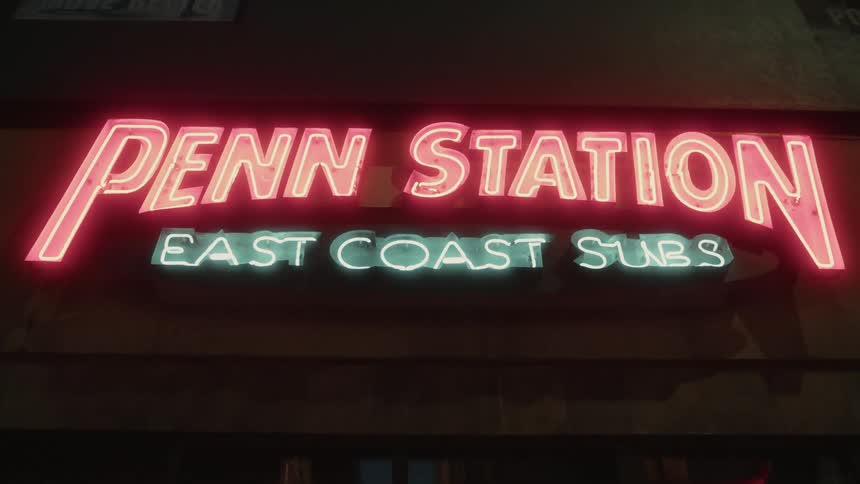 Neon sign for the penn station east coast subs restaurant glows green and red at night