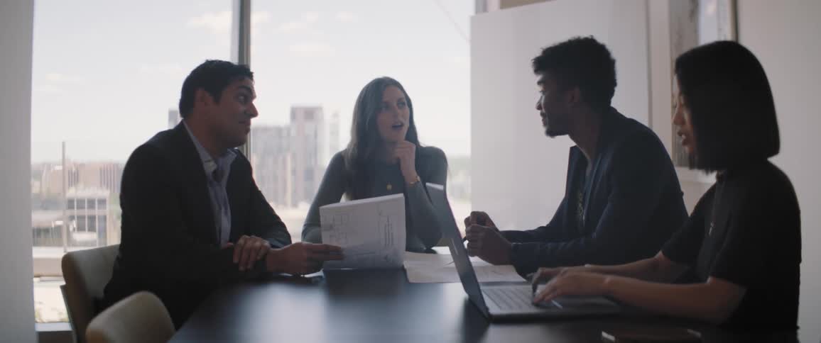 Four people including men and women sitting at a table with laptop and documents talking