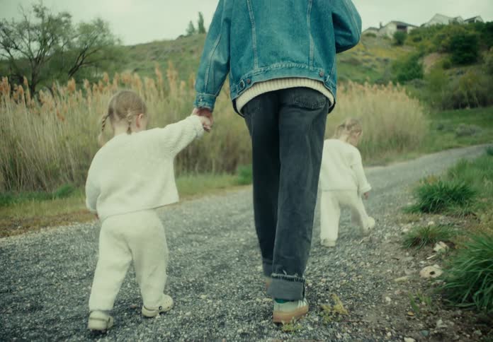 Two twin children walking with their mother on a stone street surrounded by greenery