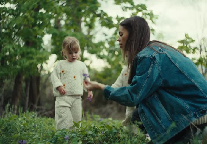 Woman picking a purple flower in a garden and showing it to her two little twin daughters