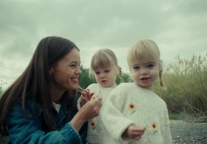 Mother crouching with her two twin daughters in a field on a cloudy day