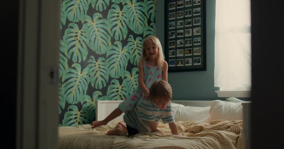 Brother and sister playing over each other on a bed in a colorful bedroom