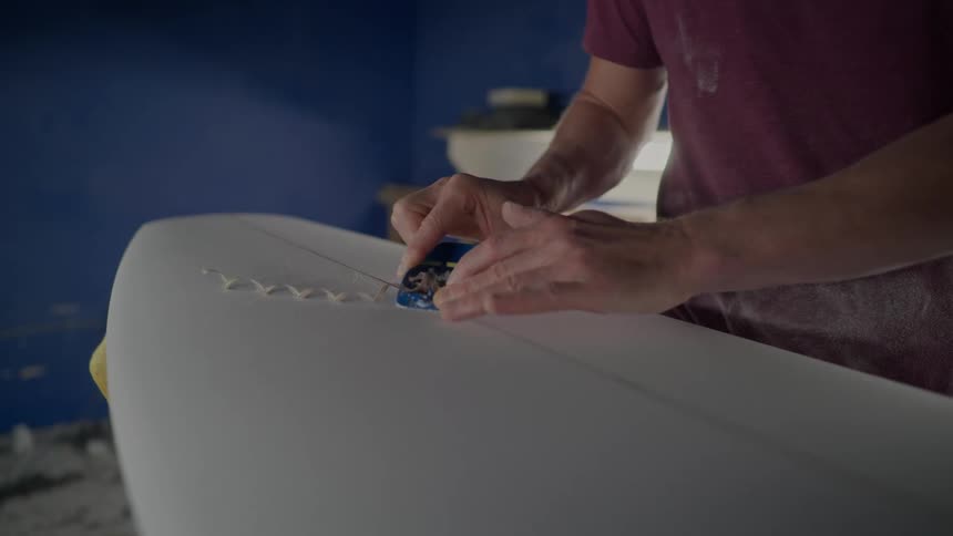 Man in a workshop working on finishing a white surfboard