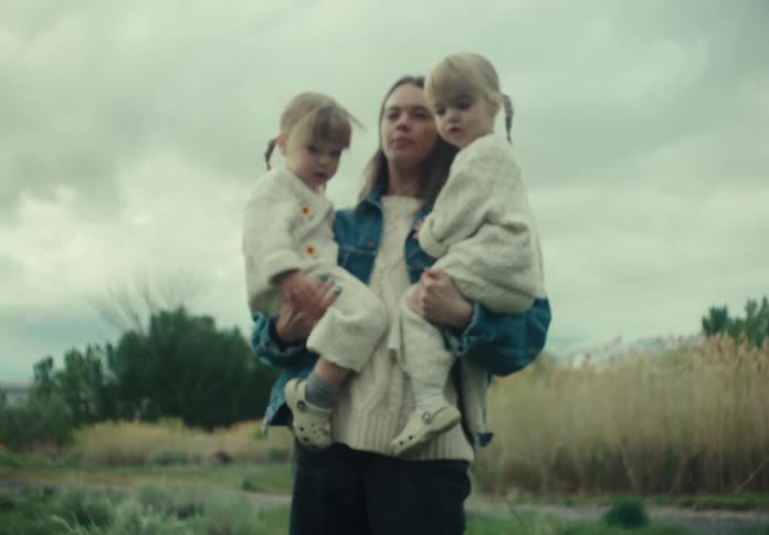 Mother picking up her two little blonde twin daughters on her lap and leading them into a field