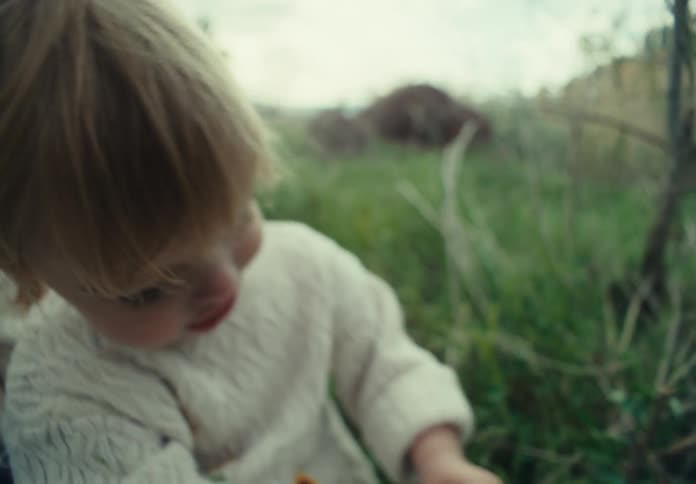 A girl wearing a knitwear sweater sitting on green grass playing next to her sister