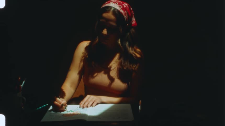 A woman wearing a head scarf draws in a notebook