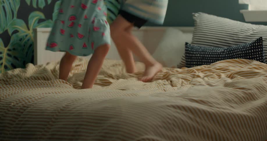 Young siblings holding hands while jumping on the bed