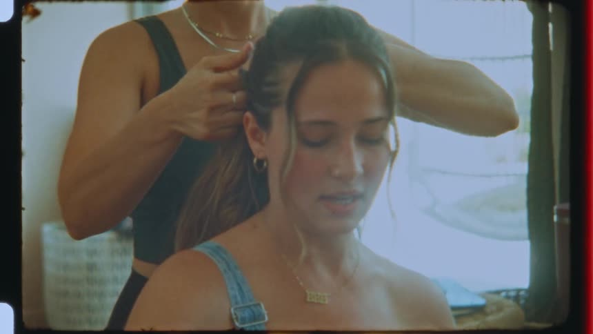 A woman styles a teenage girls hair in a room