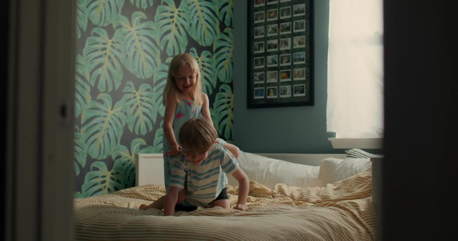Little girl on top of a boy playing on a bed smiling