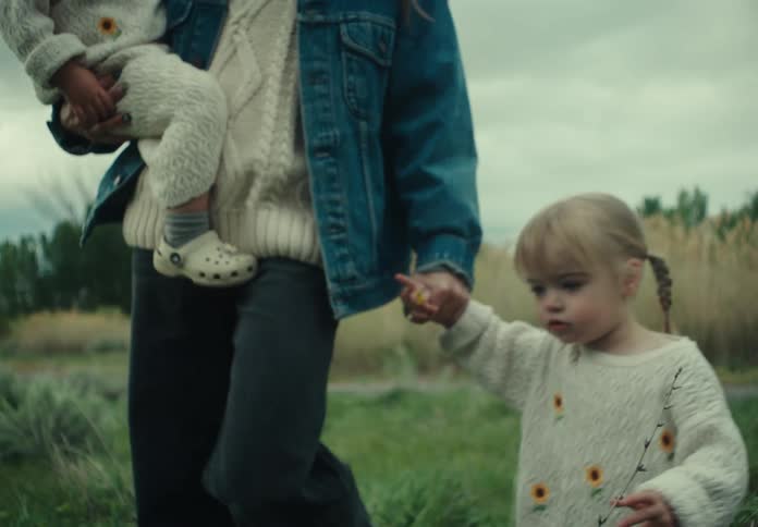 Mother walking in a field with one child on her lap and the other holding her hands