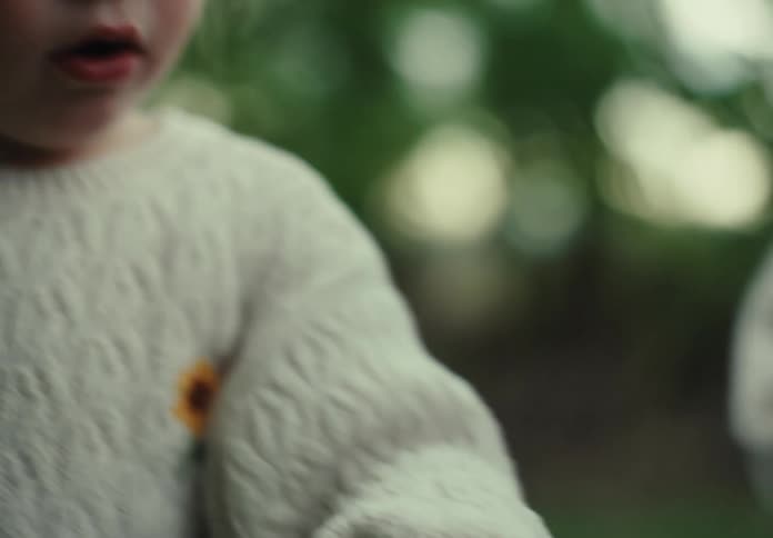 The face of a little girl wearing a white coat and she is holding a violet colored flower