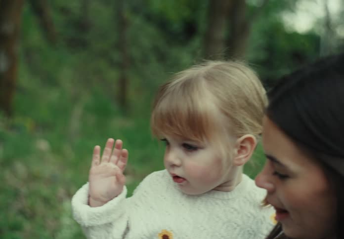 A mother walks through a nature area while holding her toddler daughter