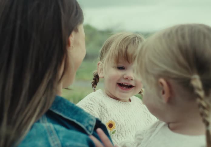 A woman wearing a denim jacket is holding two little blonde girls wearing black coats and they are both happy
