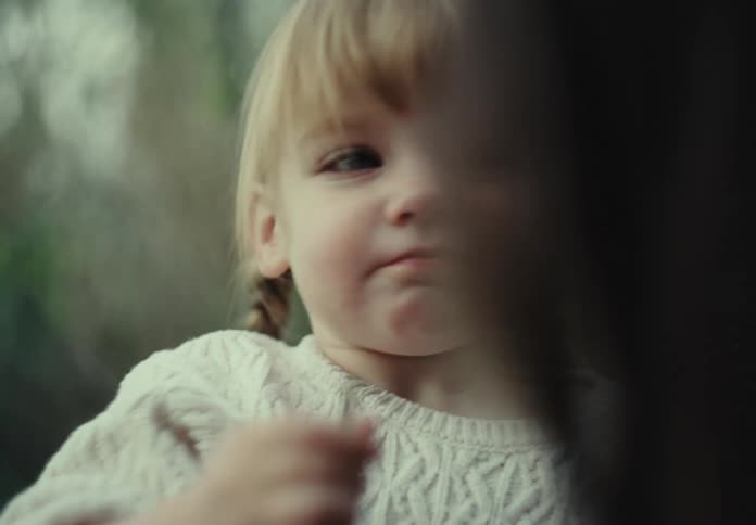 Little blonde girl sitting on her mothers lap and running her hand over her face