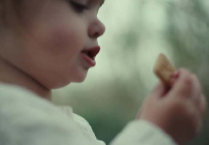 Portrait of a little girl playing with a small wooden branch and the other eating a cookie