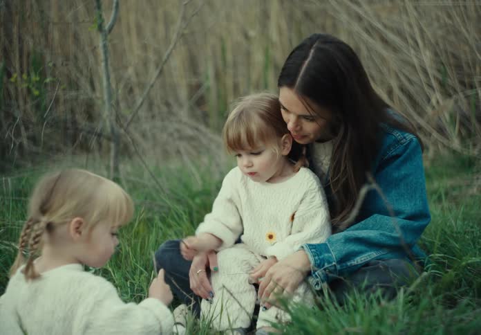 Mother and daughters sit in the grass while laughing and playing together