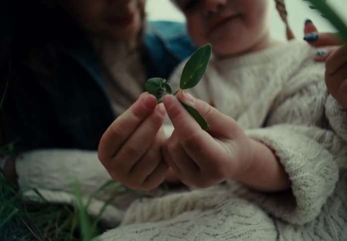 Mother sitting next to her little daughter holding green leaves