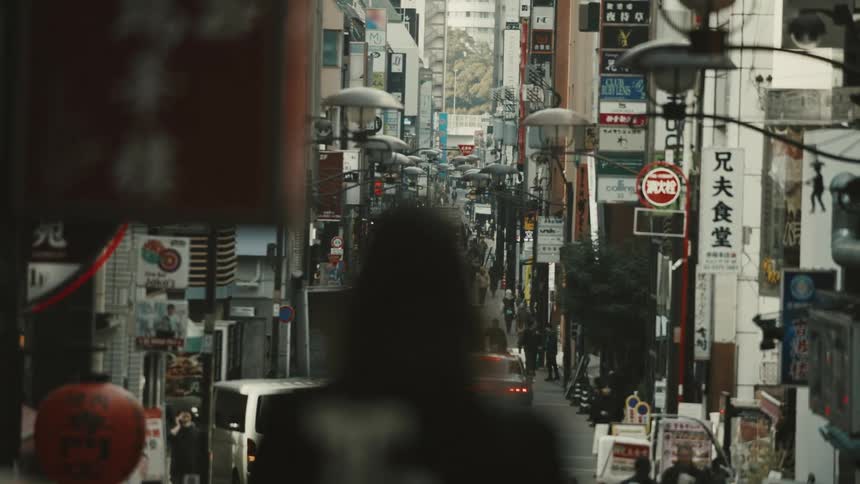 A woman walks into a busy Tokyo neighborhood filled with cars and pedestrians