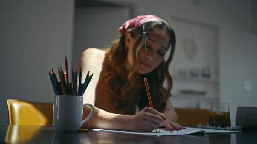 A teenage girl draws in a notebook with a pencil