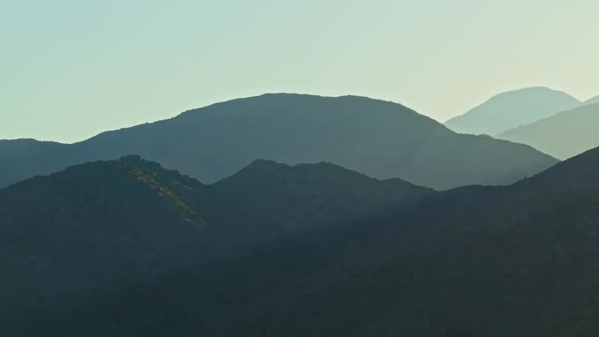 A hazy mountain range with overlapping ridges under a blue clear sky