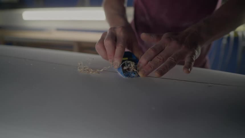 Man forms a line in a surfboard while in a workshop