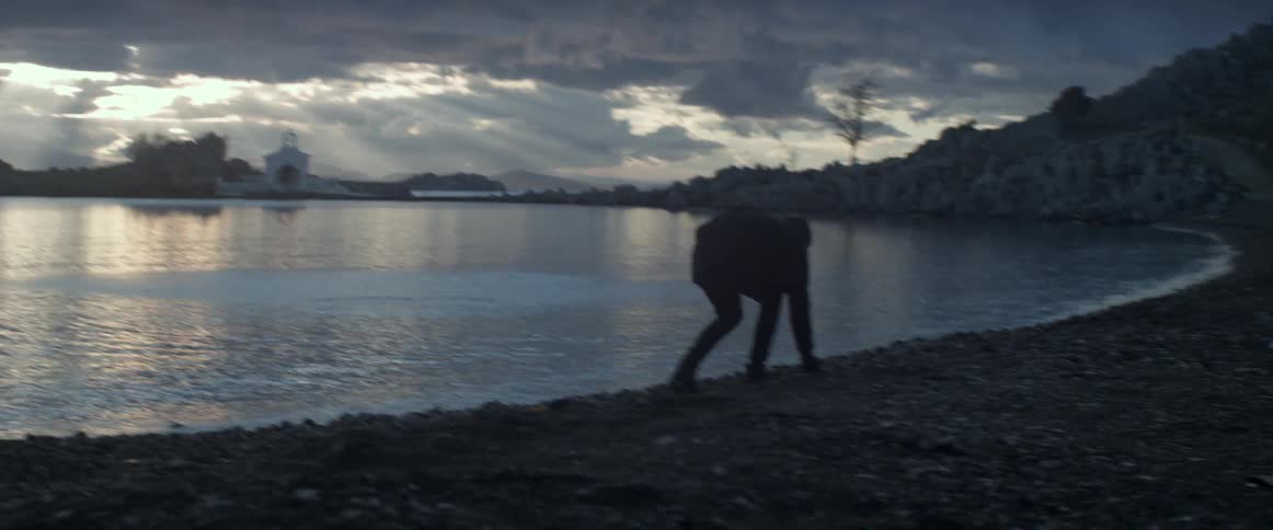 A person grabs rocks from the shore and skips them along the water