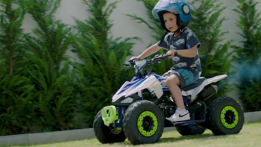 Boy smiles while chasing his younger sibling who is riding a four wheel vehicle