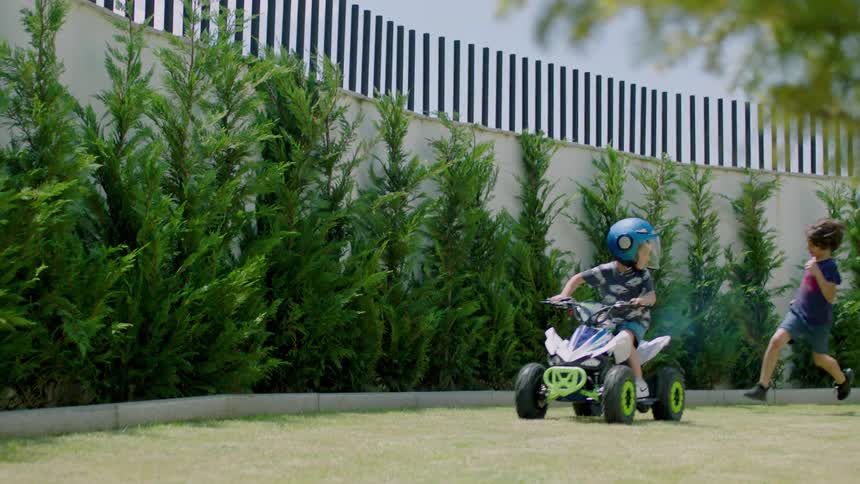 Two children running after another child who is riding an atv on grass