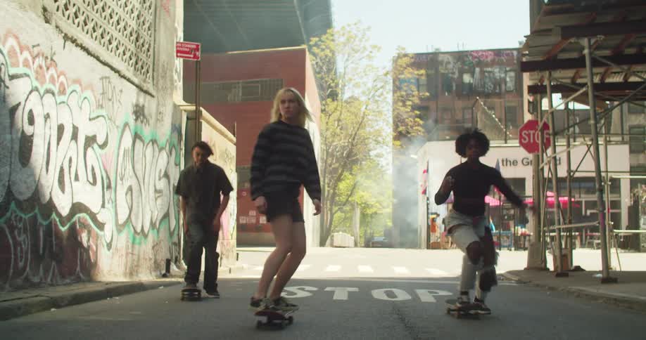Three teenagers skateboarding towards the camera on a city street decorated with graffiti