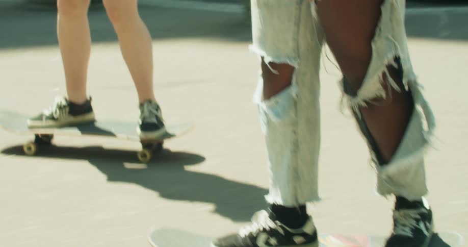 Two young women skateboarding on the sidewalk through a metropolis