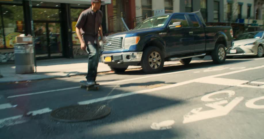 A young man jumps his skateboard into a vehicle lined city street