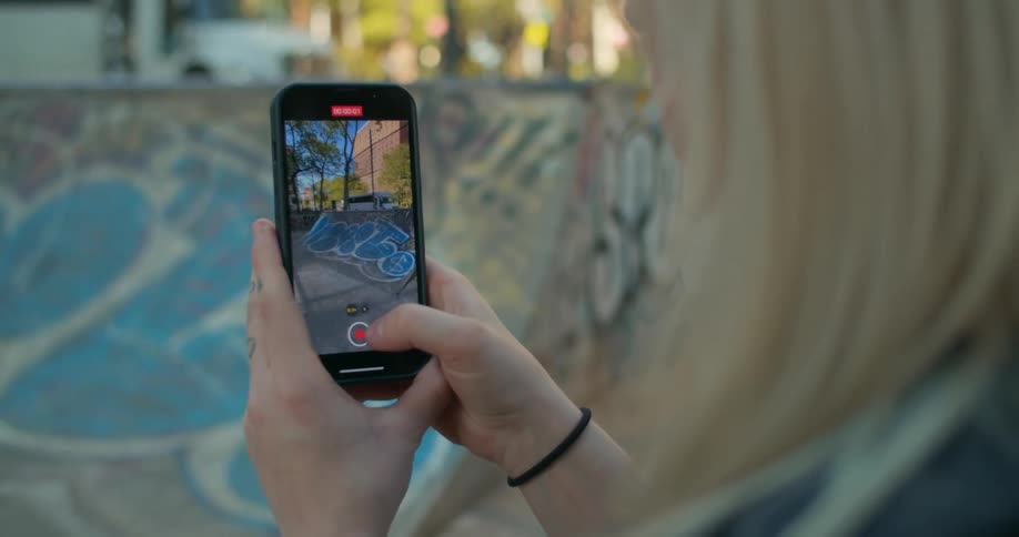 Pair of hands holding an iphone that is recording a video of a person doing a skateboarding trick