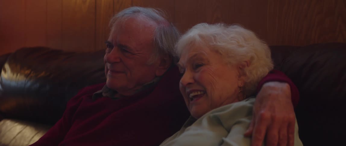 Elderly couple watches a show while cuddling and talking