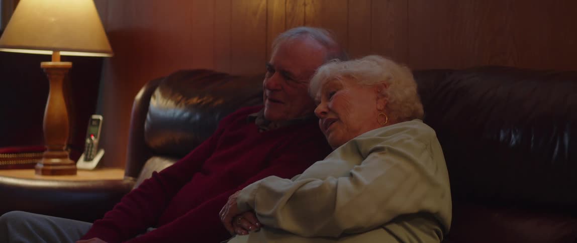Elderly couple sitting hugging each other on a sofa in the living room