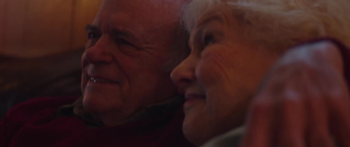 Elderly couple hugs while sitting on a couch together and smiling