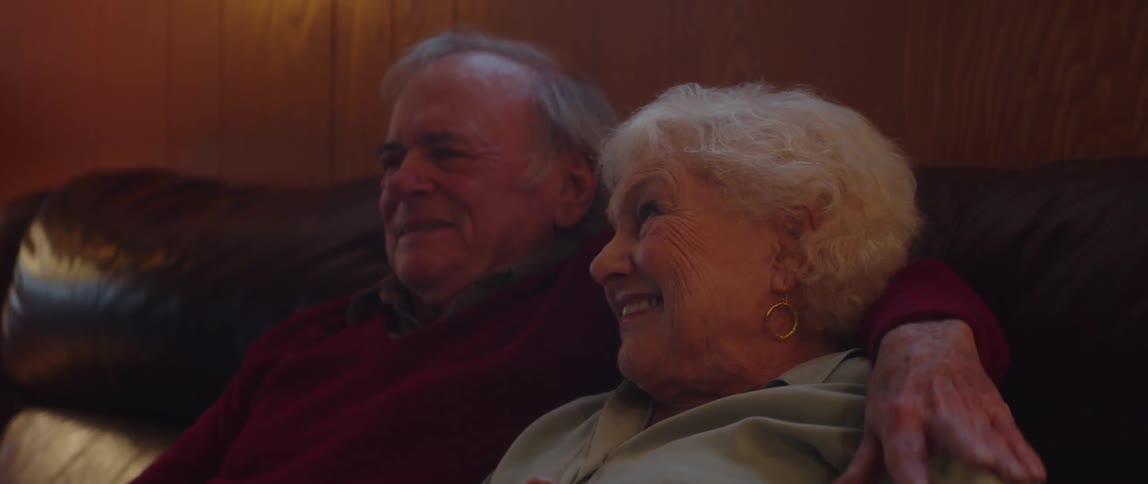 Elderly couple sitting hugging each other smiling