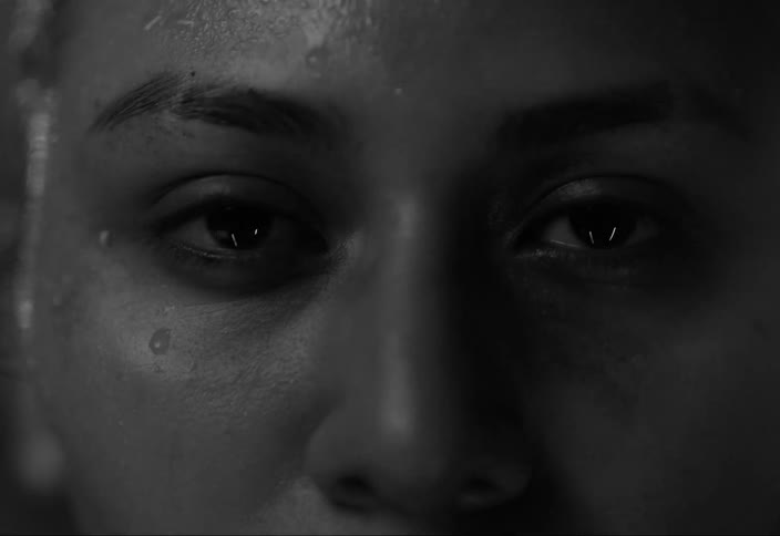 A black woman sweats and stares as a light flashes on her face