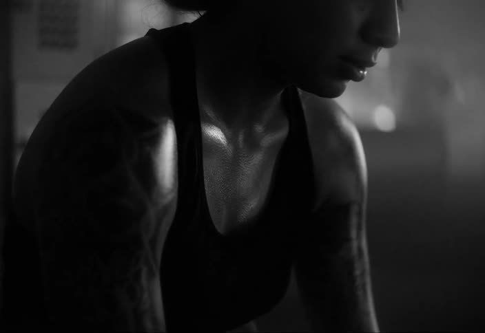 A sweaty female with tats breathes hard in a gym