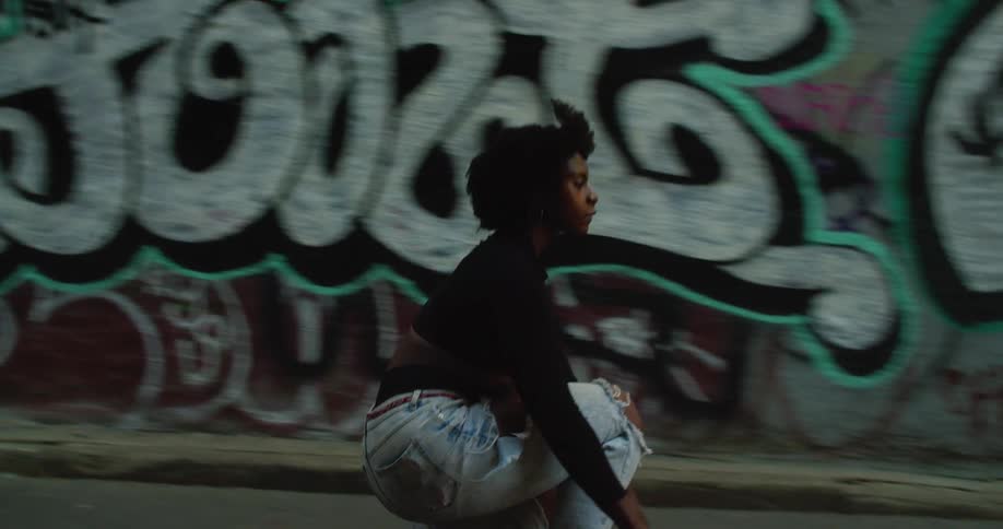 Young black woman skateboards on the road in front of an urban graffiti wall