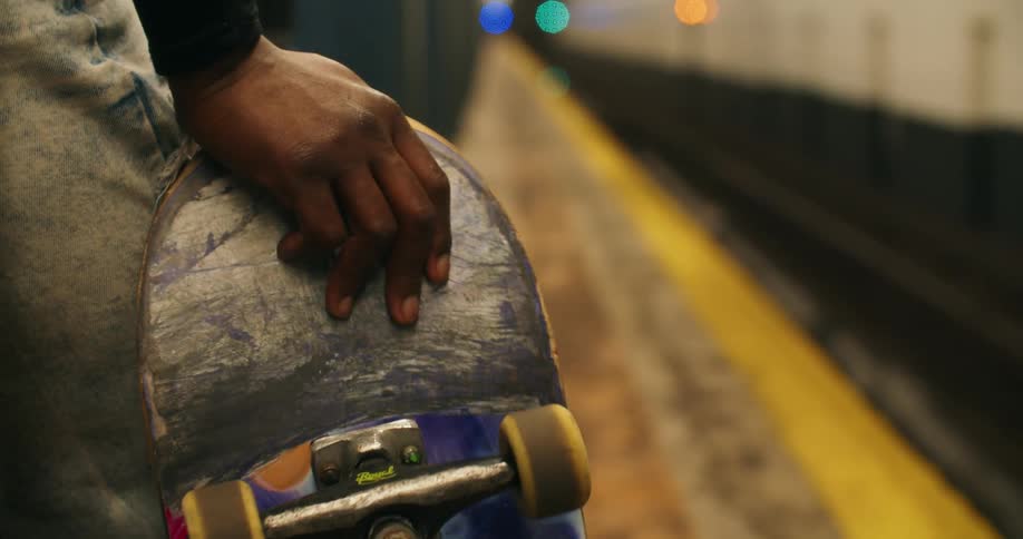 A black female holds a skateboard while waiting for a subway train