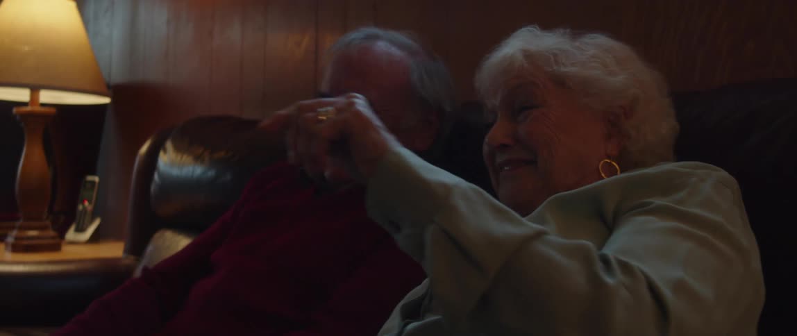 An elderly couple laugh while sitting on a couch