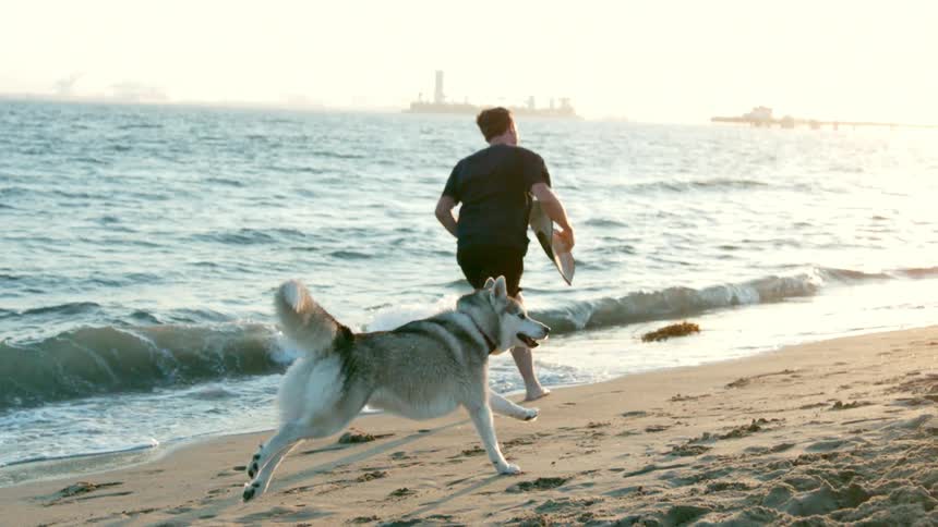 Man running on the beach sand with his dog by his side