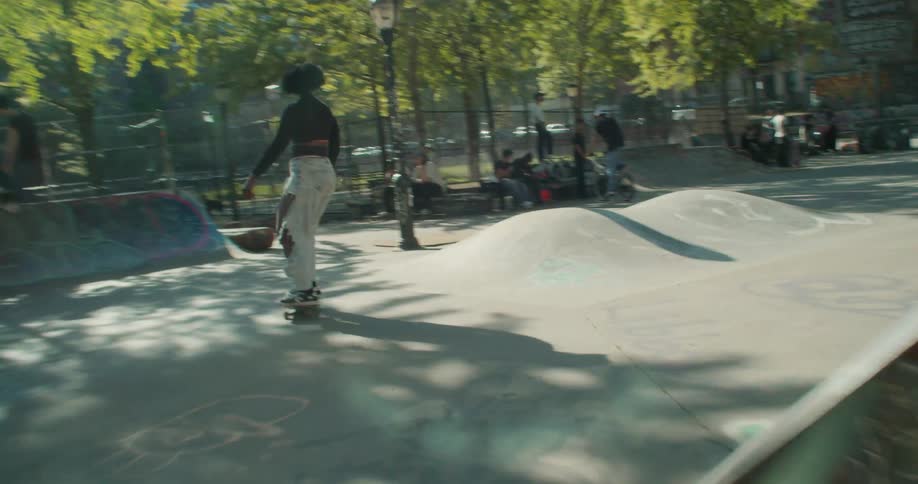 A black woman skateboards through a park filled with people