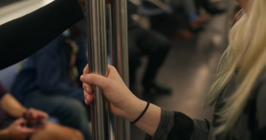 Closeup of peoples hands holding onto a metal support on a moving train