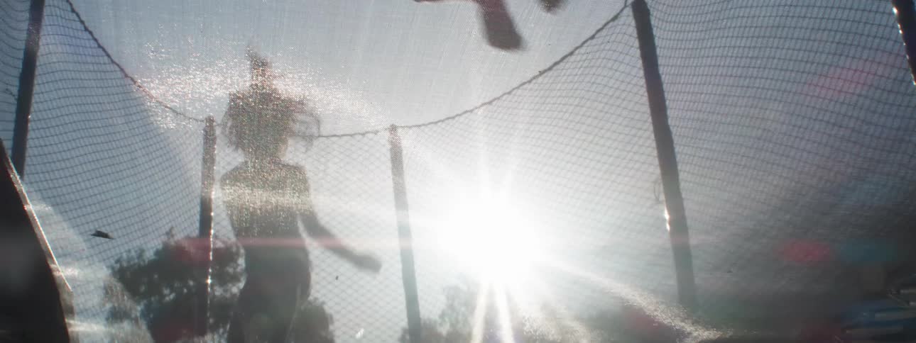 Two girls in silhouette jump on a trampoline and aggravate a dog