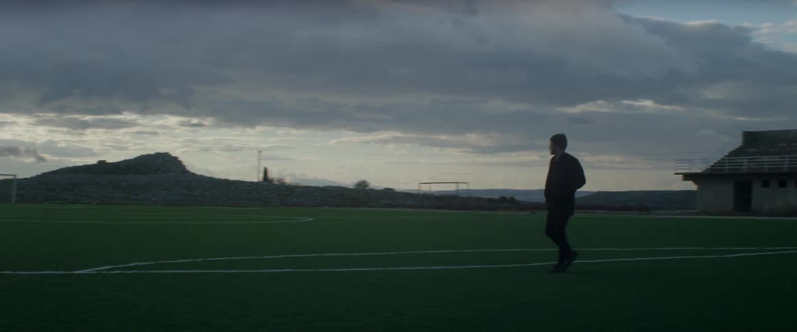 Man walking along a soccer field during a cloudy day