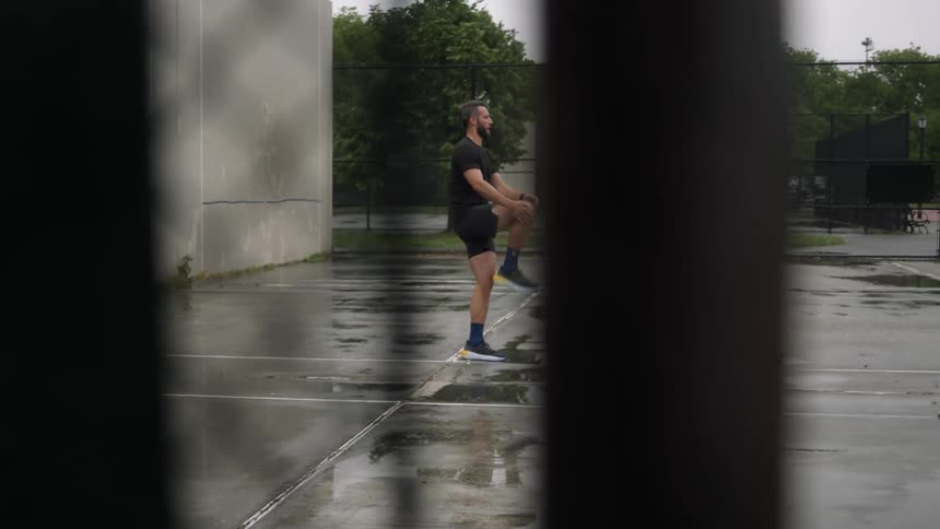 A man stretches his legs while standing on a wet court