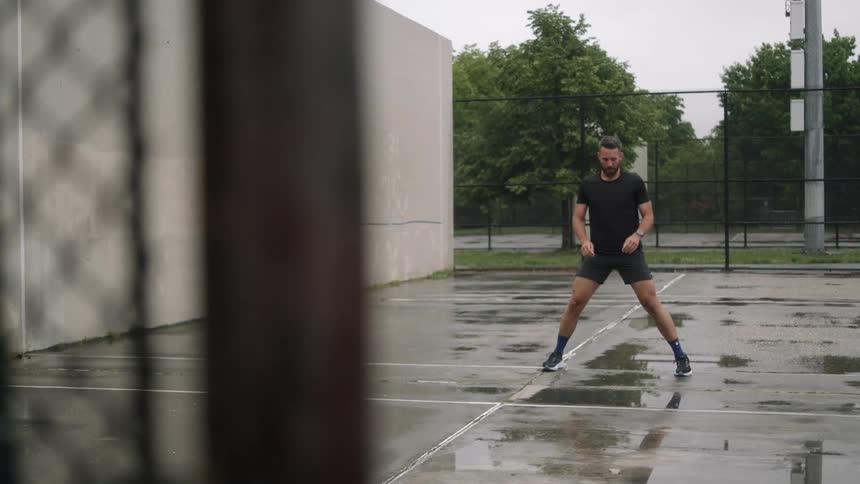 A man kneels to stretch his legs on a wet outdoor court