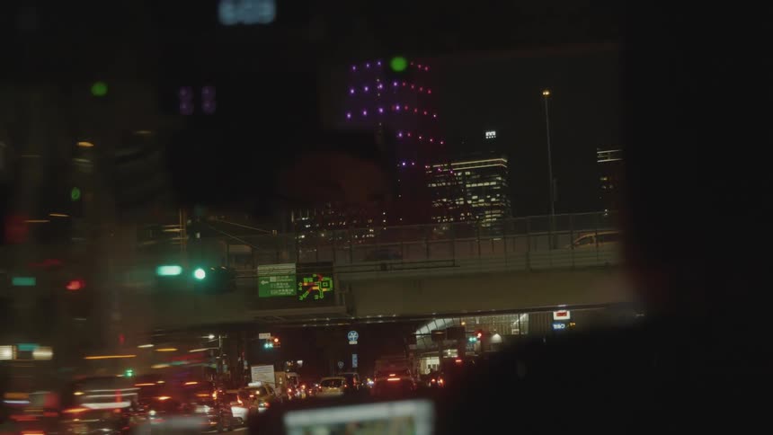 A nighttime cityscape seen from inside a vehicle driving on the streets